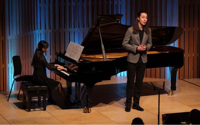 A singer stood in front of a pianist playing a grand piano.