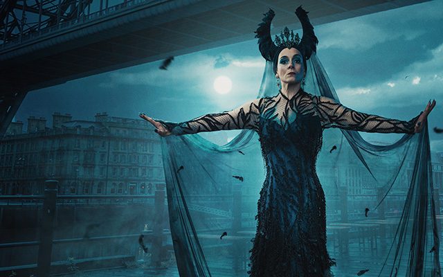 A woman with a horned-styled crown stood in front of a bridge