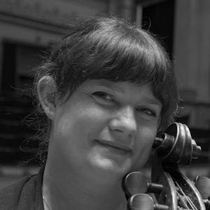 A woman smiling with the top of a cello beside her face.