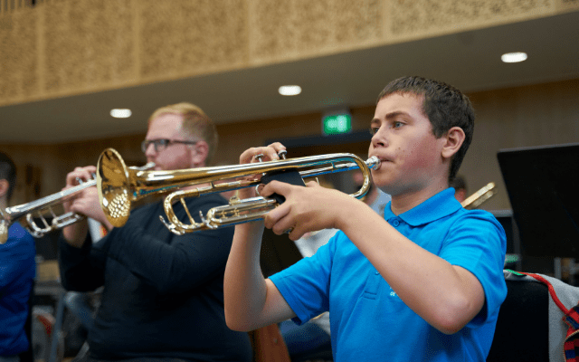 Two teenage boys play trumpets surrounded by the acoustic panelling of a music studio