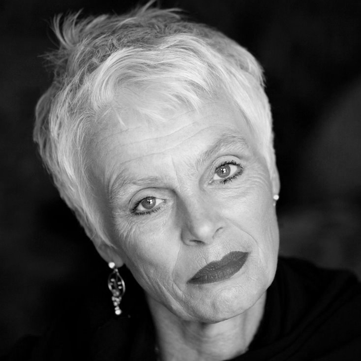 A woman with short white hair wearing large earrings.