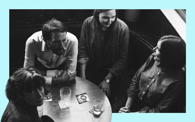A black and white image of three women and a man sitting around a wooden table