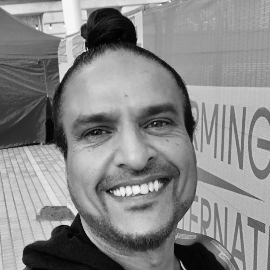 A man is looking into the camera and smiling. His hair is tied up in a bun.